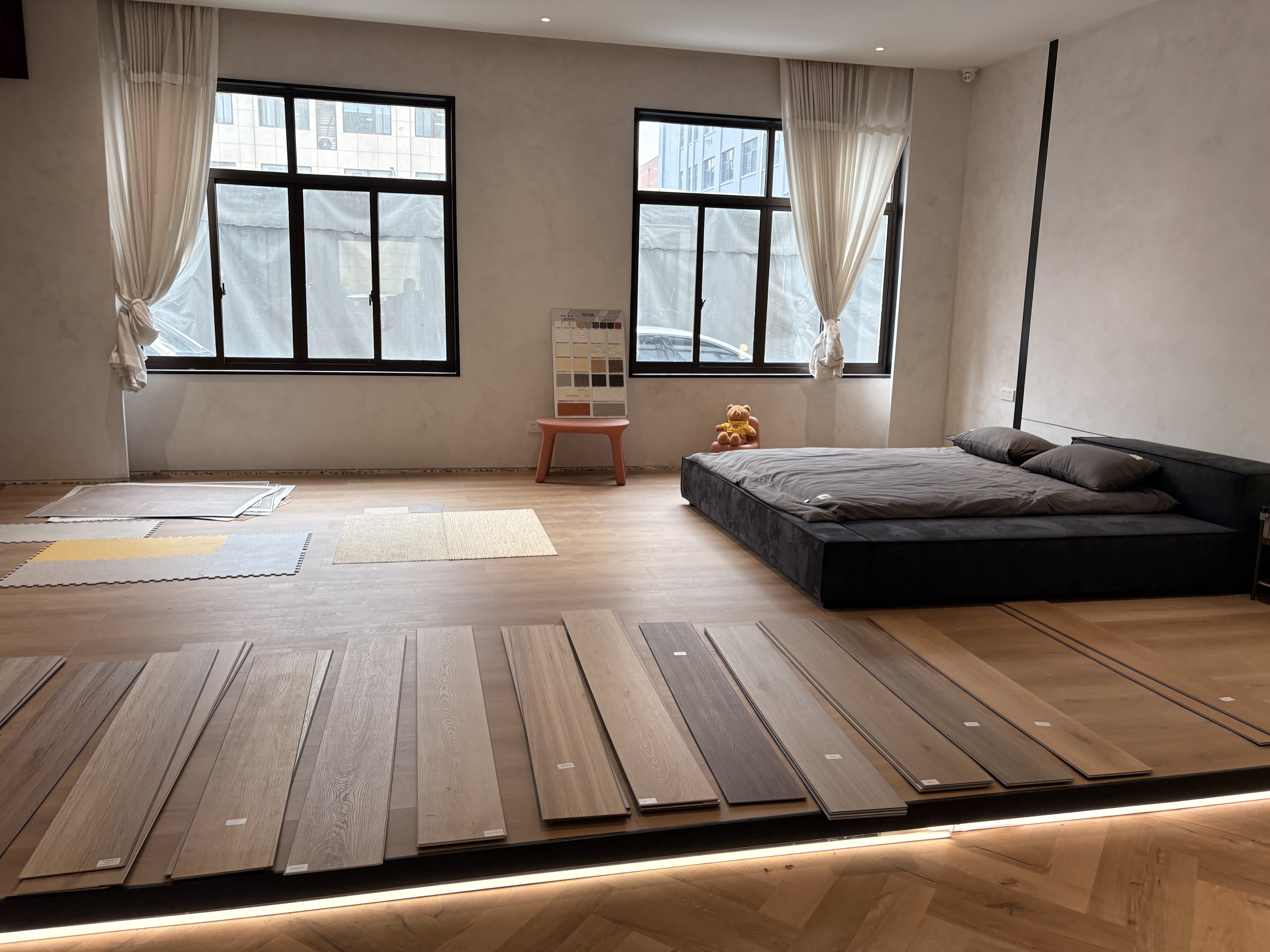 Bedroom-style showroom setup with flooring samples laid out around a low bed